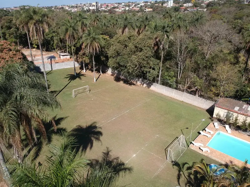 Campo de futebol gramado com duas traves, visto do alto, com piscina e espreguiçadeiras no canto