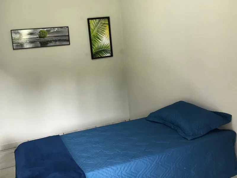 Quarto com cama de solteiro de colcha azul e dois quadros na parede
